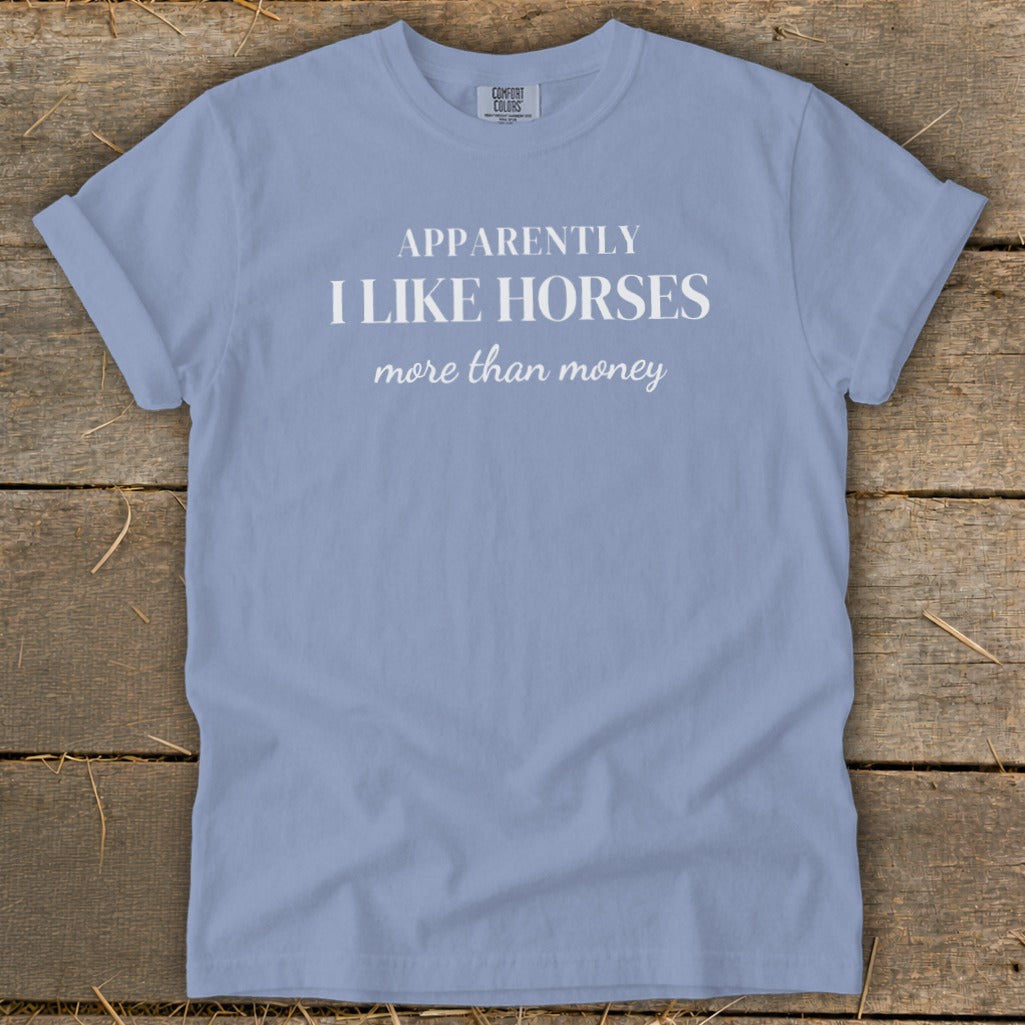 Light blue t-shirt with white text: "APPARENTLY I LIKE HORSES more than money".