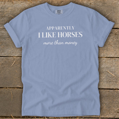 Light blue t-shirt with white text: "APPARENTLY I LIKE HORSES more than money".