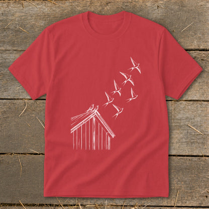 A red crewneck t-shirt featuring a white line drawing of birds flying from a small wooden building.