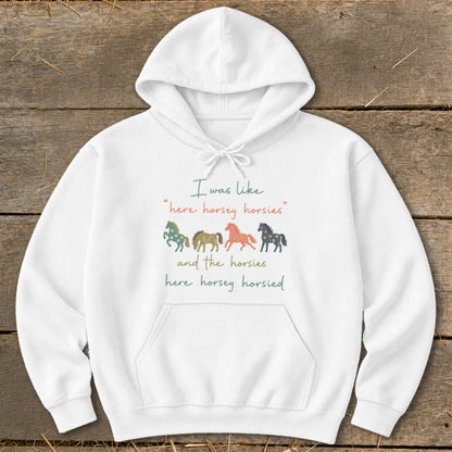 White hoodie with "I was like 'here horsey horsies'" text and four colorful horses.