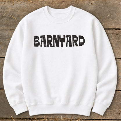 A white crewneck sweatshirt featuring the black distressed text BARNYARD centered across the chest, laid flat on a rustic wooden background.