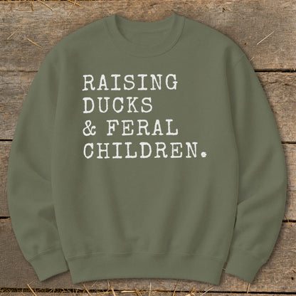 Green crewneck sweatshirt with white text reading "RAISING DUCKS & FERAL CHILDREN."