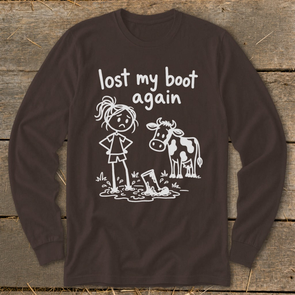 A dark brown long-sleeve t-shirt with a white stick-figure graphic showing a person and a cow next to a boot stuck in mud, with the text "lost my boot again".