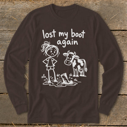 A dark brown long-sleeve t-shirt with a white stick-figure graphic showing a person and a cow next to a boot stuck in mud, with the text "lost my boot again".