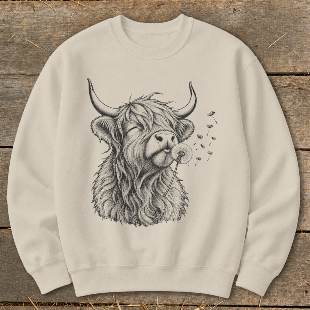 Cream sweatshirt with a sketch of a Highland cow blowing dandelion seeds.