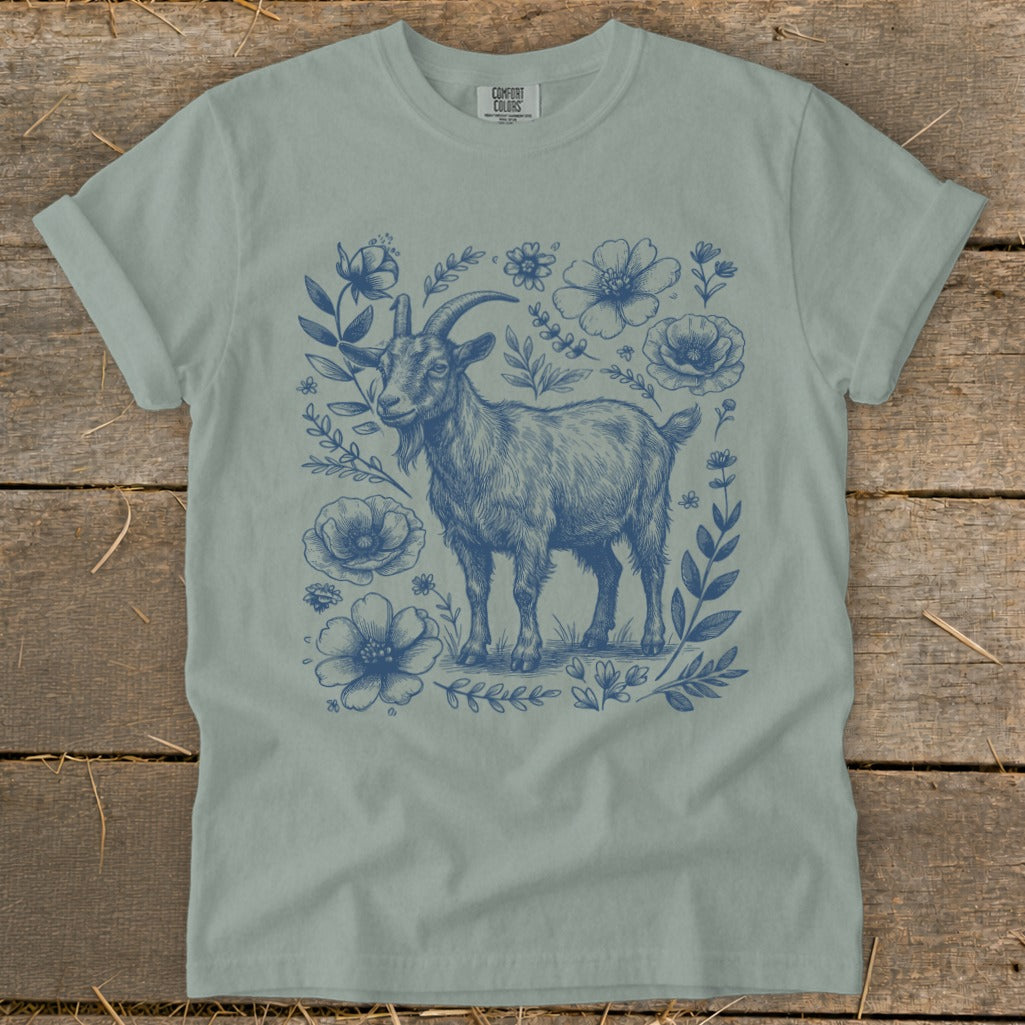 Blue ink drawing of a goat surrounded by flowers on a light blue t-shirt.