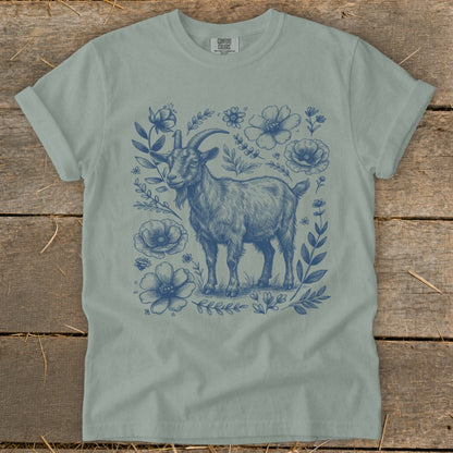 Blue ink drawing of a goat surrounded by flowers on a light blue t-shirt.