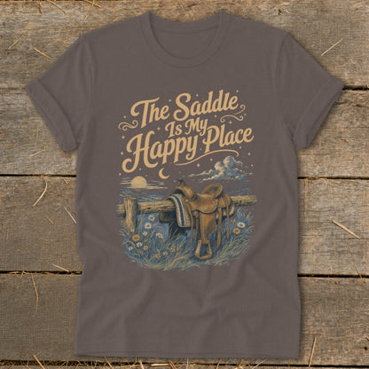 Brown t-shirt with graphic of a saddle on a fence and text "The Saddle Is My Happy Place".