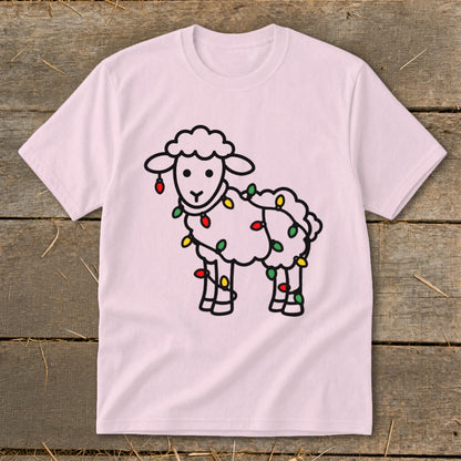 A light pink t-shirt displays a black-outline graphic of a sheep wrapped in colorful holiday lights.