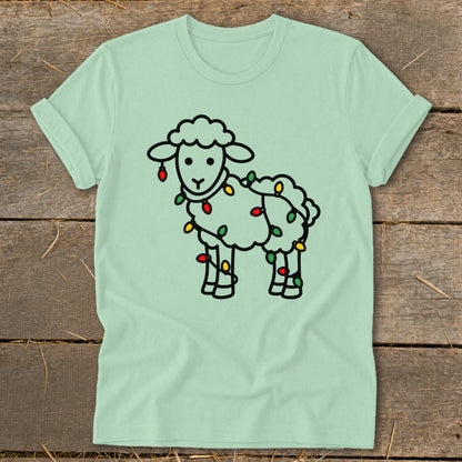 Mint green t-shirt featuring a cartoon sheep tangled in colorful Christmas lights, displayed on a wooden background.