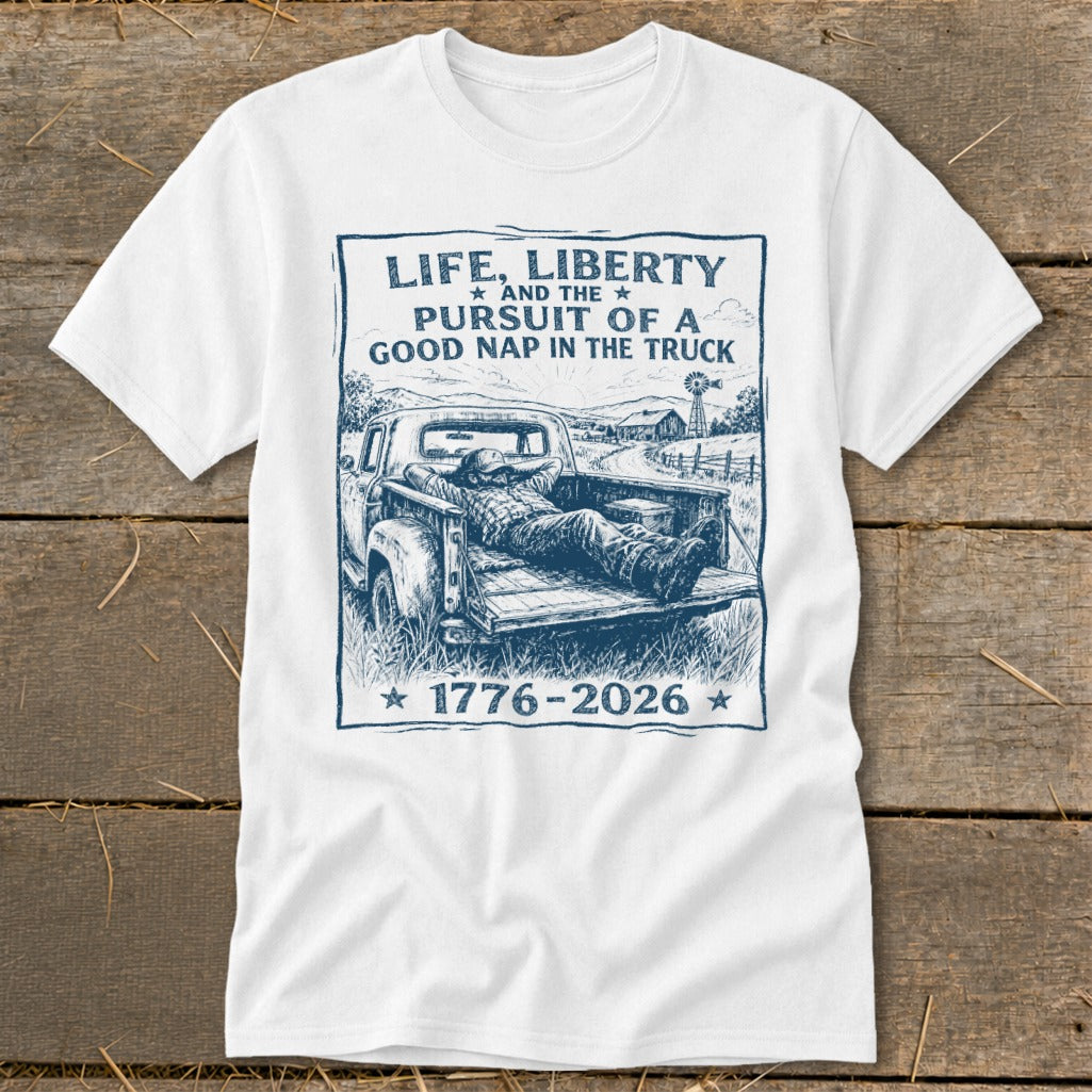 White t-shirt with blue graphic of man napping in truck bed, quote: Life, Liberty, Pursuit of a Good Nap.