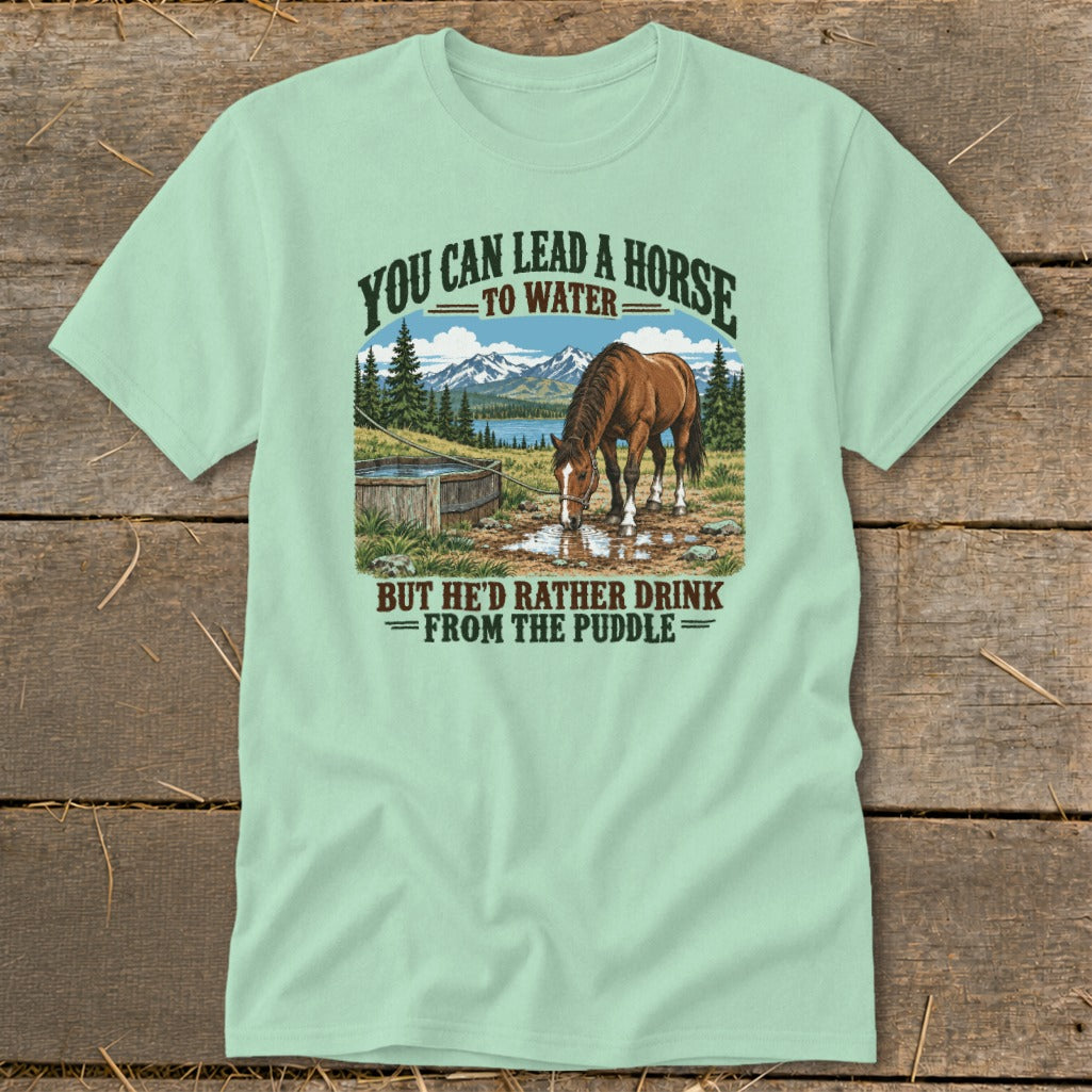 A light green t-shirt with a vintage graphic of a horse drinking from a puddle and the text YOU CAN LEAD A HORSE TO WATER BUT HE'D RATHER DRINK FROM THE PUDDLE.