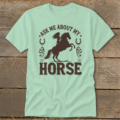 Light mint t-shirt with brown graphic of a woman riding a rearing horse and text "ASK ME ABOUT MY HORSE".