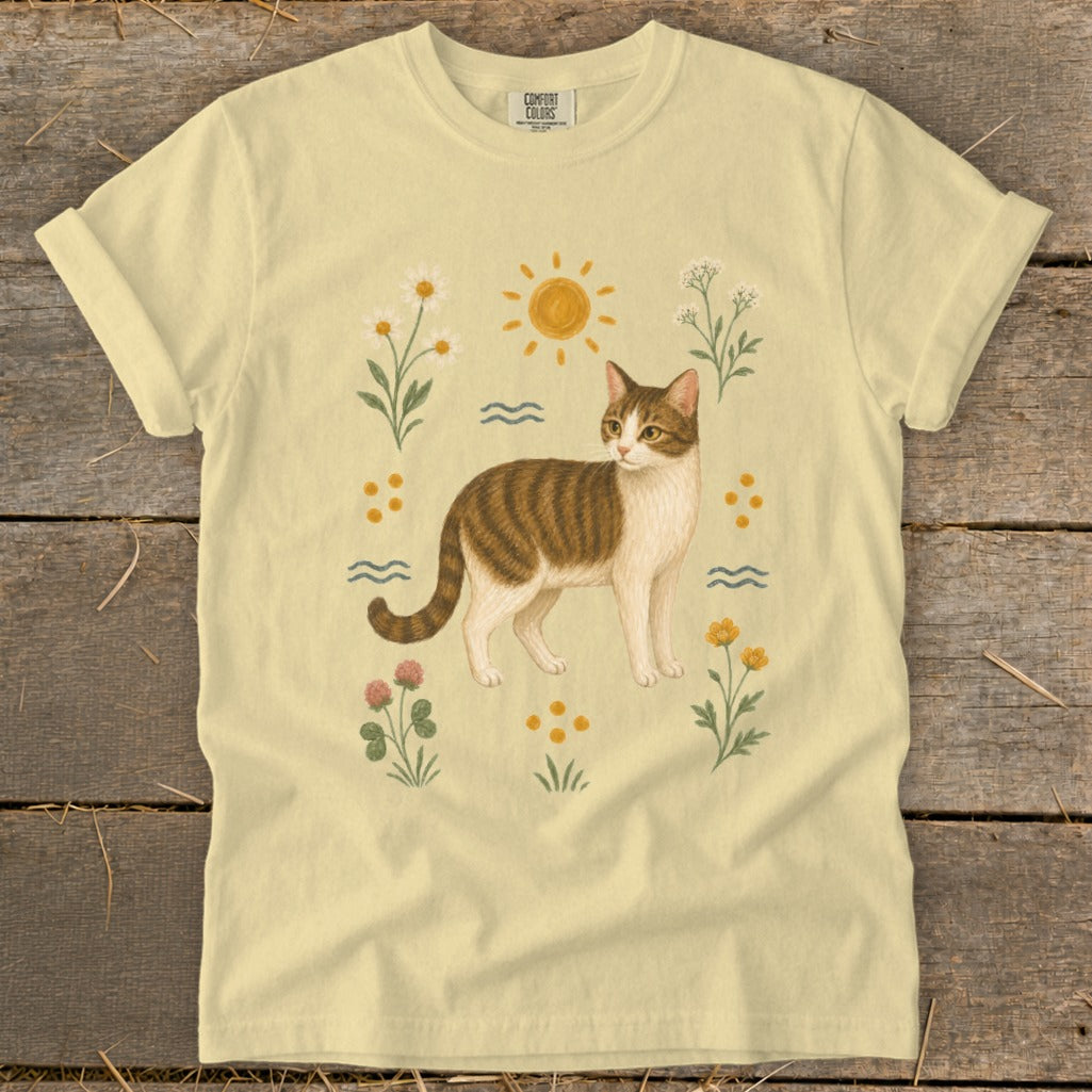 Yellow t-shirt with a tabby cat illustration surrounded by flowers and sun.