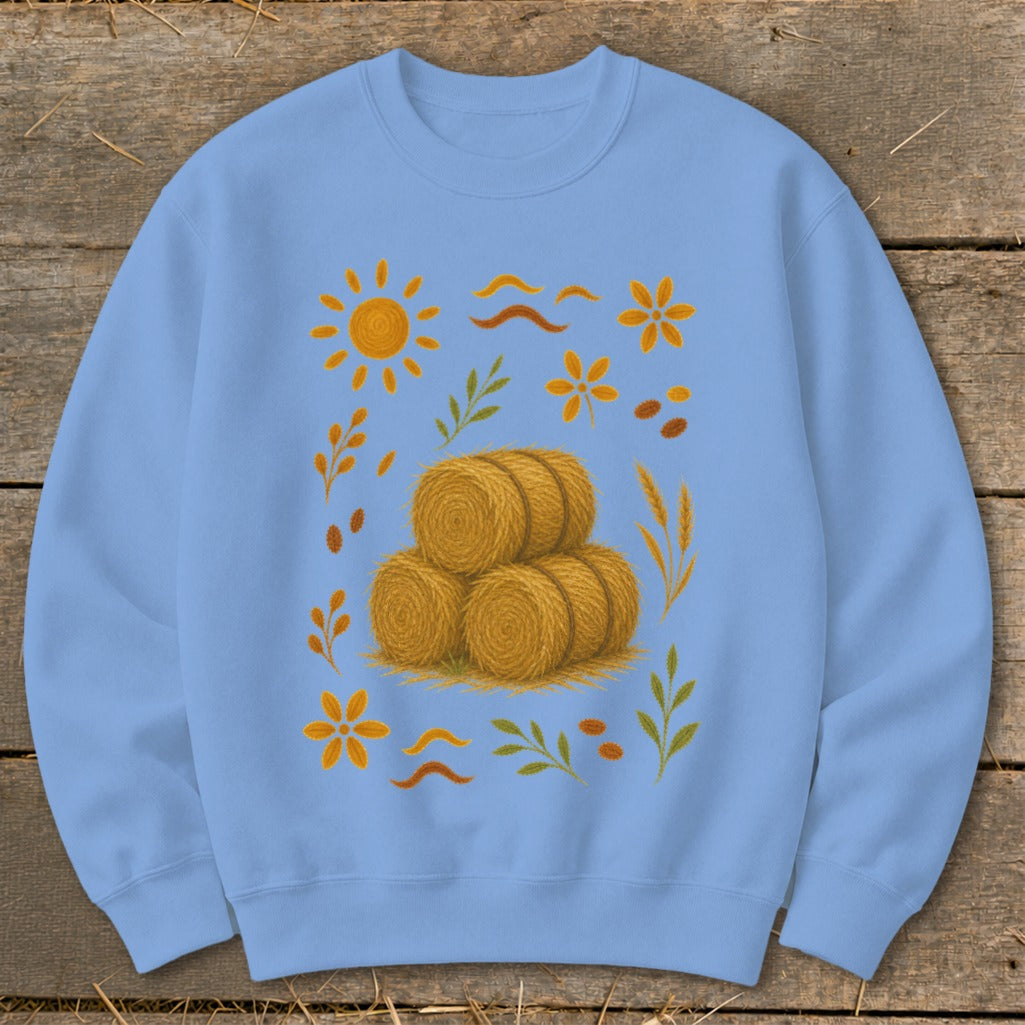 Light blue sweatshirt with a fall harvest graphic featuring hay bales, sun, and autumn leaves.