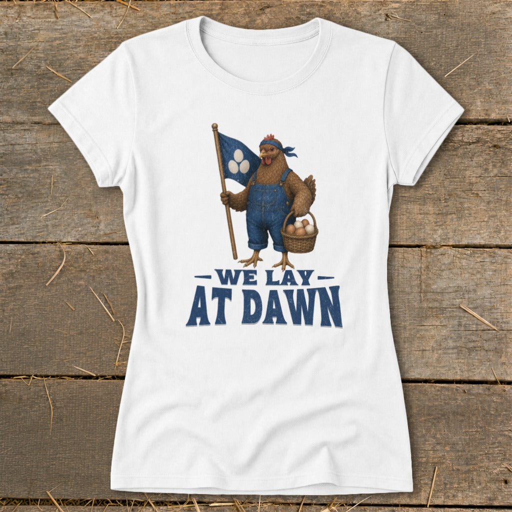 White t-shirt with a chicken holding a flag and basket, text reads "WE LAY AT DAWN".
