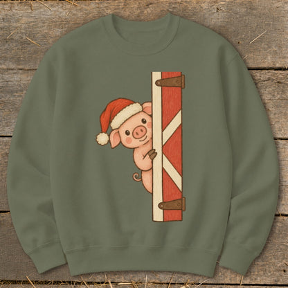 Pig in Santa hat peeks around a red barn door on a green sweatshirt.