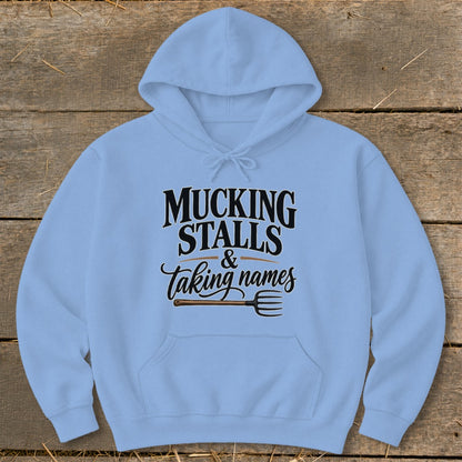 Light blue hoodie with text "MUCKING STALLS & taking names" and a pitchfork.