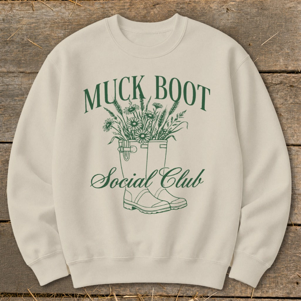 Cream sweatshirt with green "Muck Boot Social Club" graphic featuring boots and flowers.