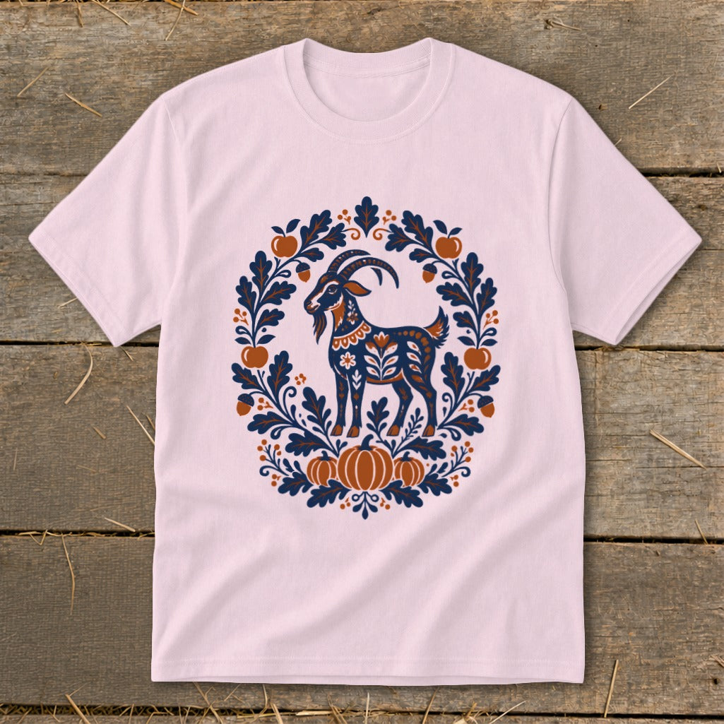 Light pink short-sleeved t-shirt featuring a folk-art graphic of a goat surrounded by autumn leaves, apples, and pumpkins.