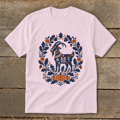 Light pink short-sleeved t-shirt featuring a folk-art graphic of a goat surrounded by autumn leaves, apples, and pumpkins.