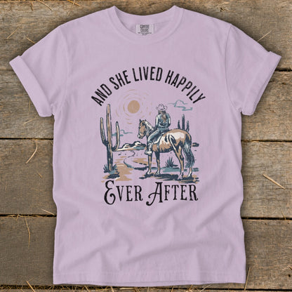 Lavender t-shirt with woman on horse in desert scene and text "And She Lived Happily Ever After".