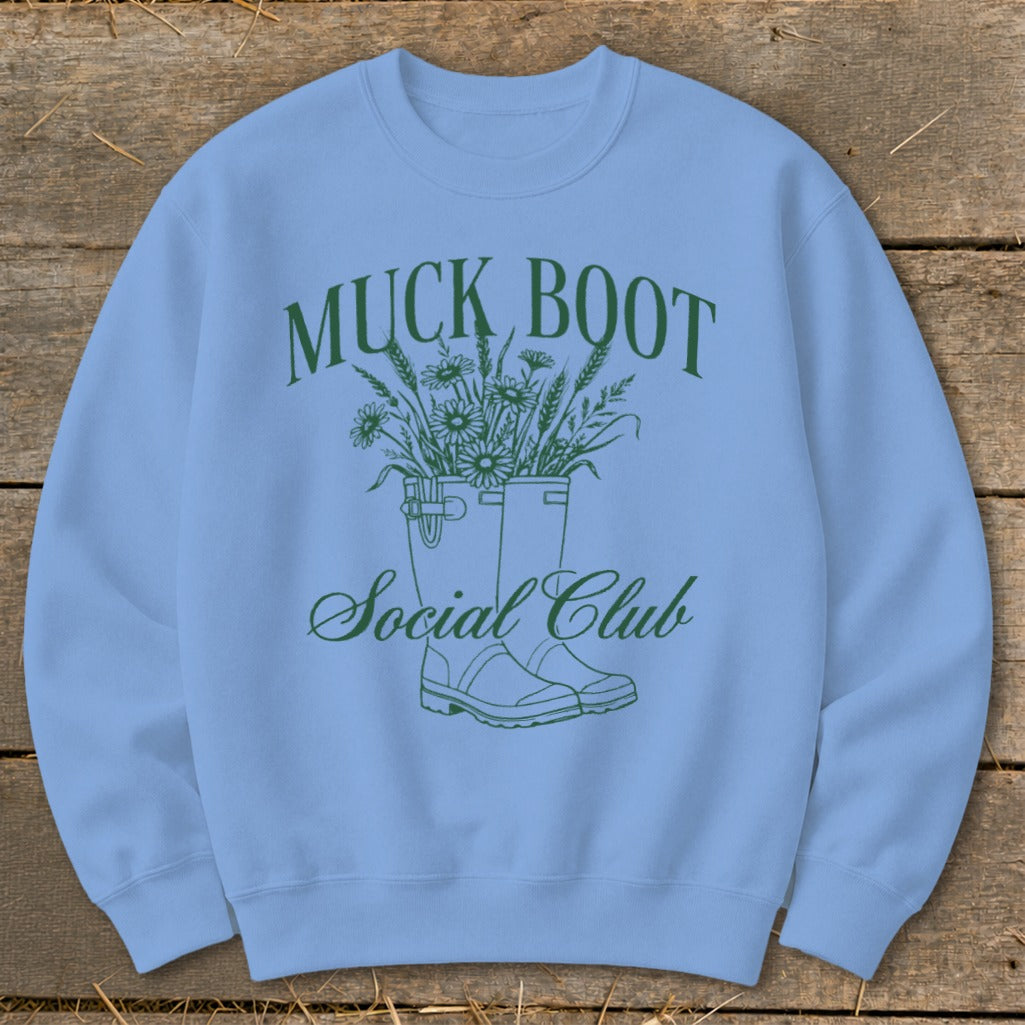Light blue sweatshirt with green "Muck Boot Social Club" text and floral boot design.