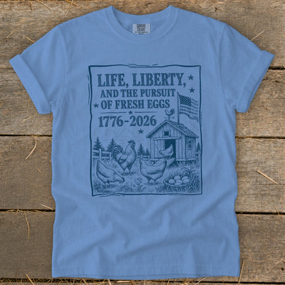 Light blue t-shirt with "Life, Liberty, and the Pursuit of Fresh Eggs 1776-2026" graphic.