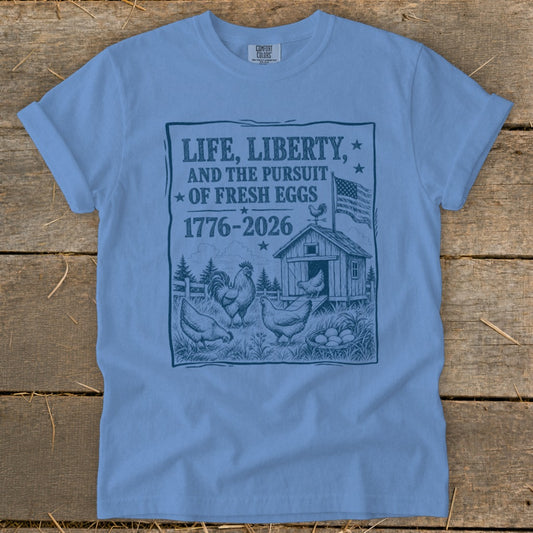 Light blue t-shirt with "Life, Liberty, and the Pursuit of Fresh Eggs 1776-2026" graphic.