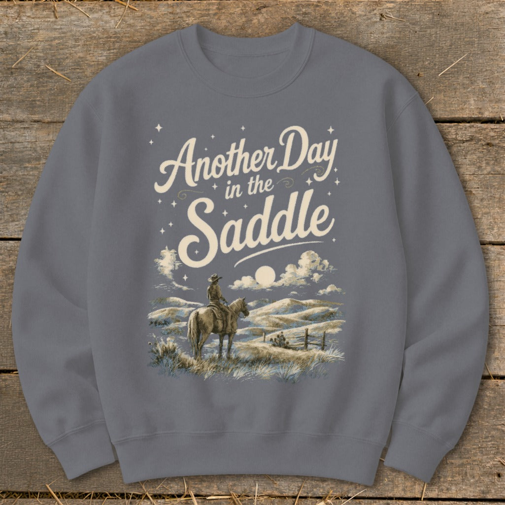 Sweatshirt with "Another Day in the Saddle" text and a cowboy on horseback in a landscape.