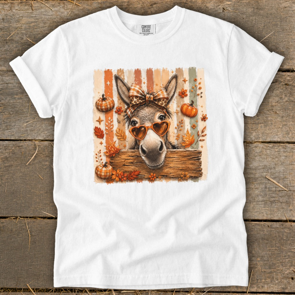 Donkey wearing heart sunglasses and bow, surrounded by pumpkins and autumn leaves.