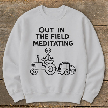 White sweatshirt with "Out in the field meditating" text and a stick figure meditating on a tractor.