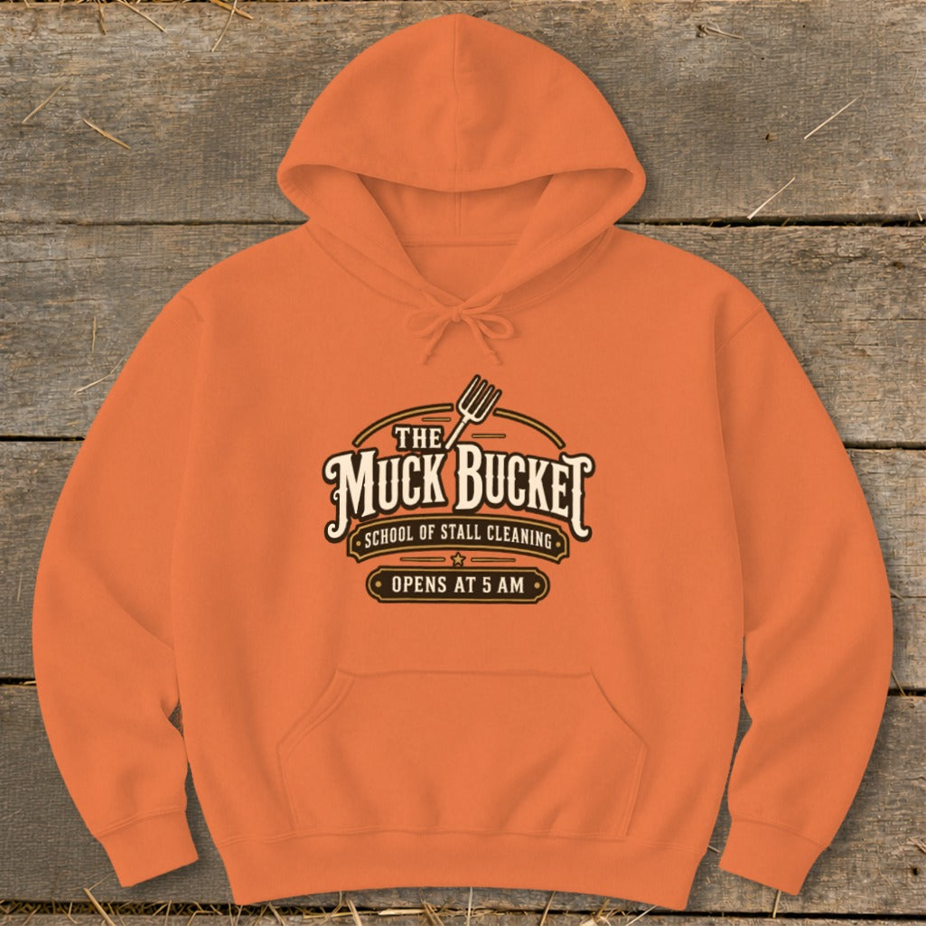 Orange hoodie with "The Muck Bucket School of Stall Cleaning Opens at 5 AM" logo.