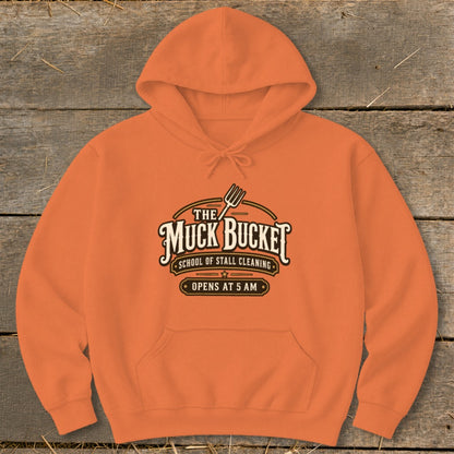 Orange hoodie with "The Muck Bucket School of Stall Cleaning Opens at 5 AM" logo.