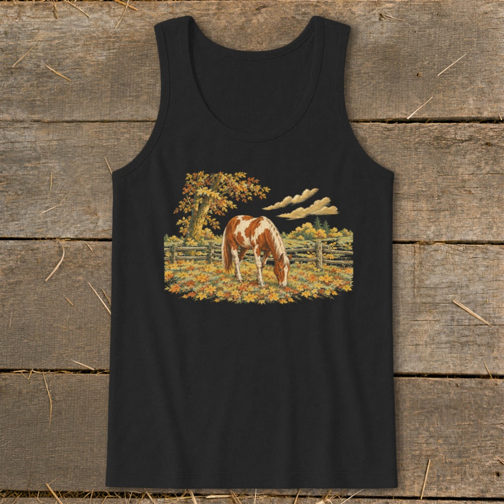 Brown and white horse grazing in a field of autumn leaves by a wooden fence.