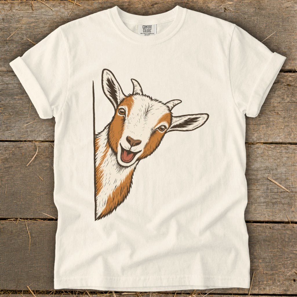 Illustration of a peeking goat with white and brown fur on a cream t-shirt.