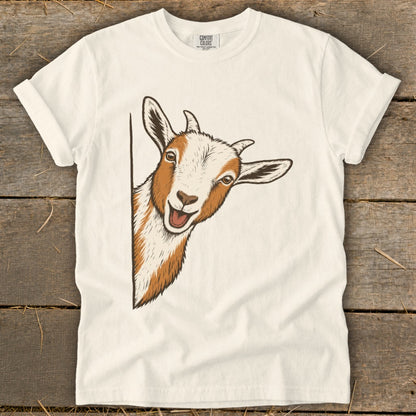 Illustration of a peeking goat with white and brown fur on a cream t-shirt.
