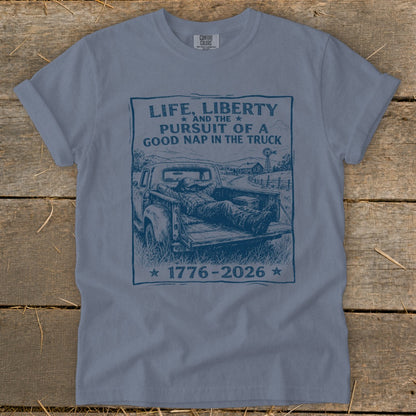 Blue t-shirt with a graphic of a man napping in a truck bed and the text "Life, Liberty... Good Nap in the Truck".