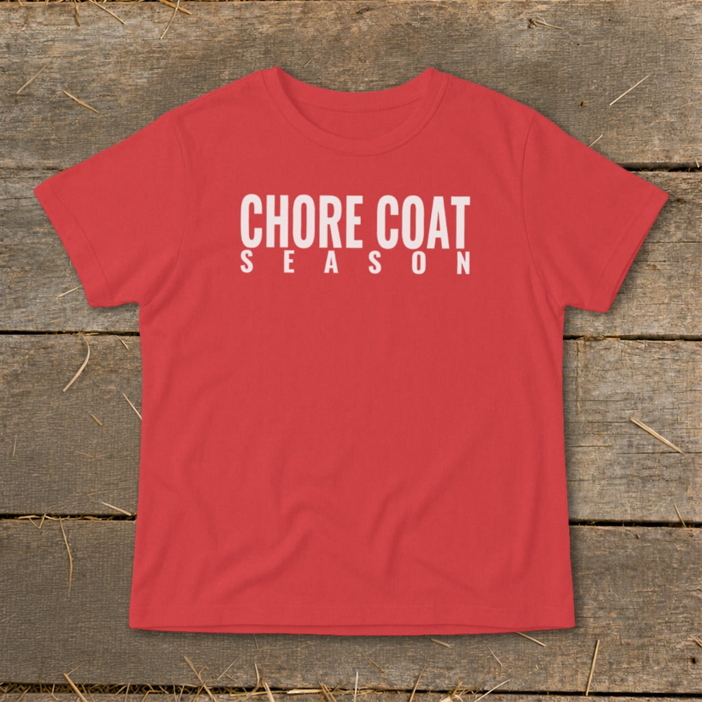 Red t-shirt with white text "CHORE COAT SEASON" on a wooden background.