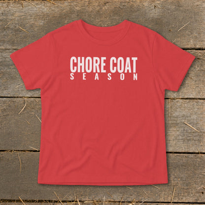 Red t-shirt with white text "CHORE COAT SEASON" on a wooden background.