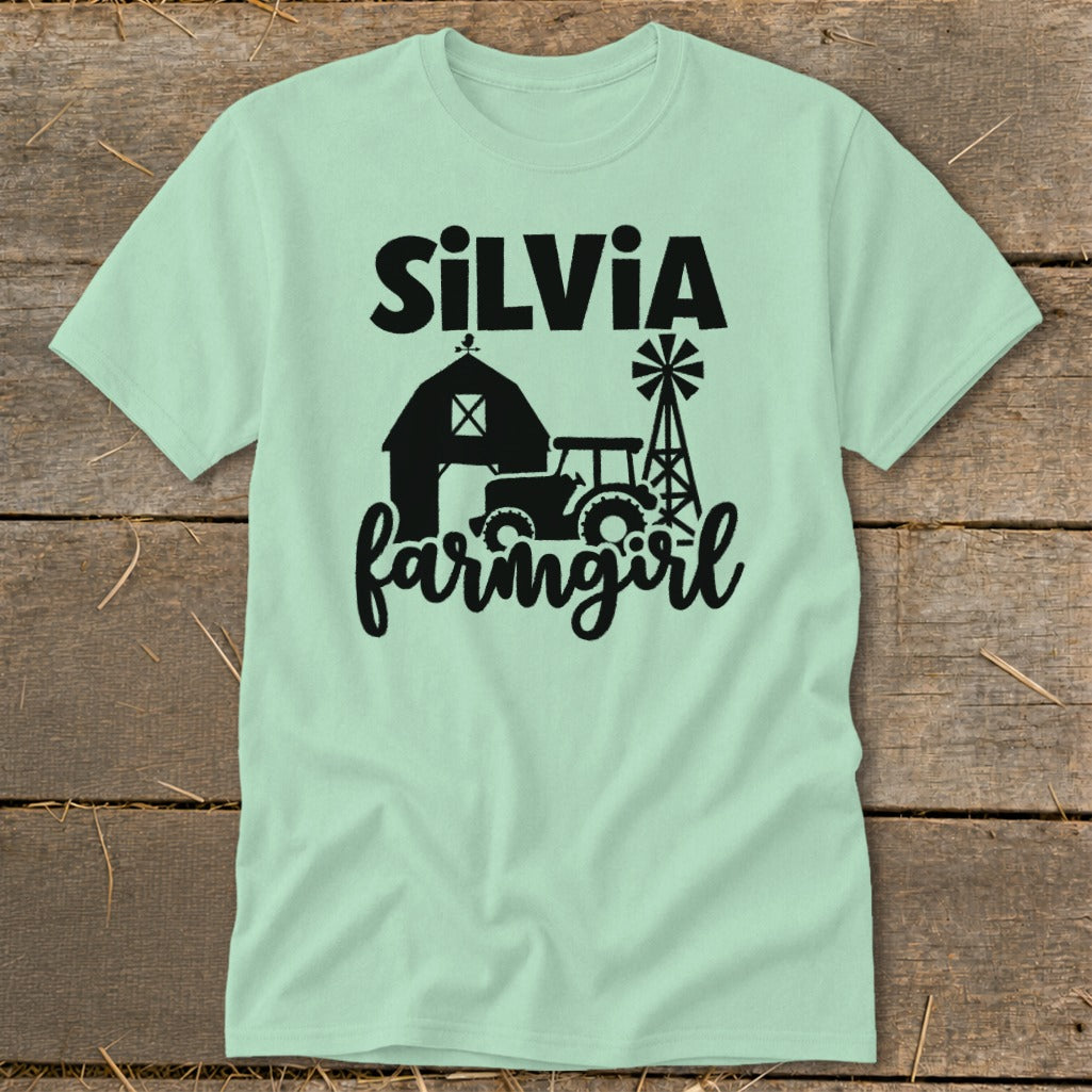 Light green t-shirt with "SiLVIA" above barn, tractor, and windmill graphic that reads "farmgirl".