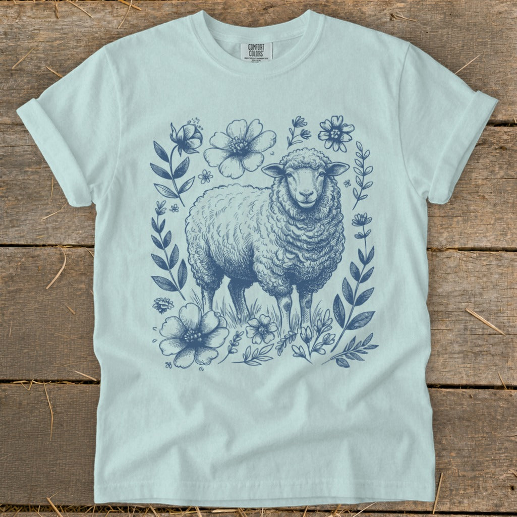 Light blue t-shirt with a detailed blue drawing of a sheep surrounded by flowers and foliage.