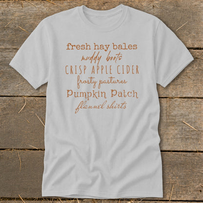 Light grey t-shirt with text: fresh hay bales, muddy boots, crisp apple cider, frosty pastures, pumpkin patch, flannel shirts.