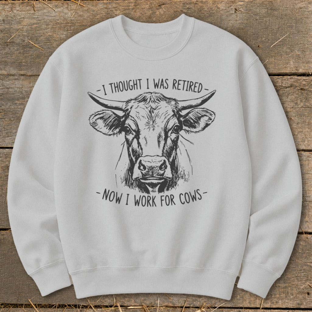 White sweatshirt with a drawing of a cow and text "I THOUGHT I WAS RETIRED - NOW I WORK FOR COWS".