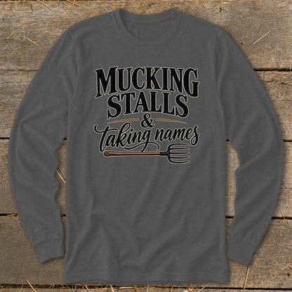 Long sleeve shirt with text "MUCKING STALLS & Taking names" and a pitchfork.