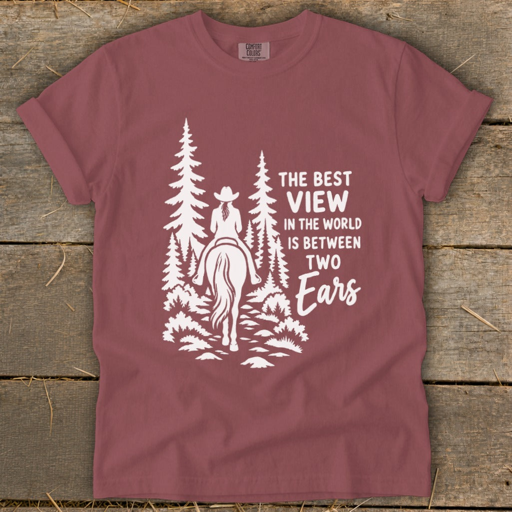 Mauve short-sleeve t-shirt with white graphic of a horse rider in trees and text reading "The best view in the world is between two ears".