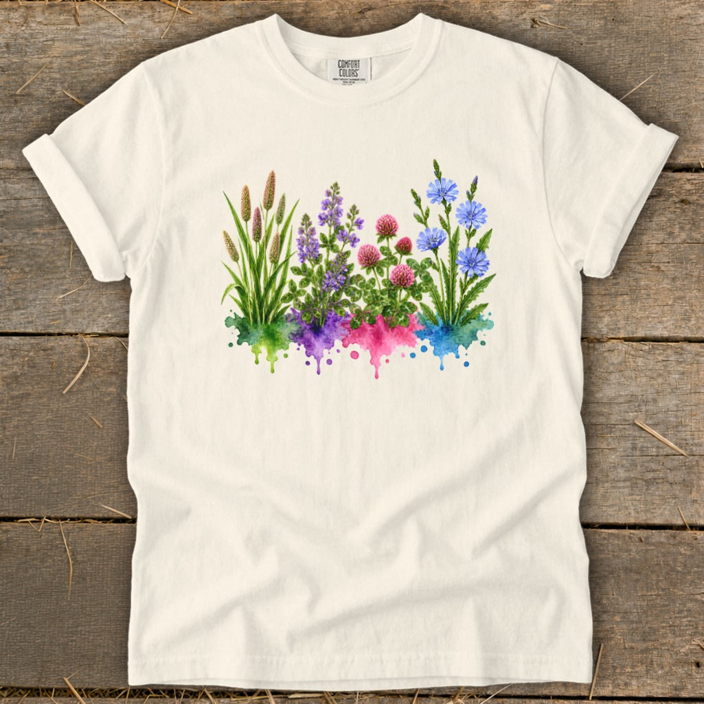 An off-white short-sleeve t-shirt features a watercolor botanical graphic with green, purple, pink, and blue flowers.