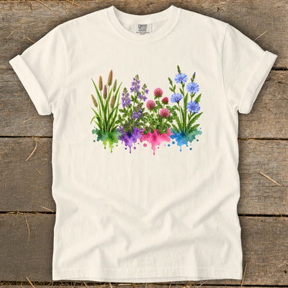 An off-white short-sleeve t-shirt features a watercolor botanical graphic with green, purple, pink, and blue flowers.
