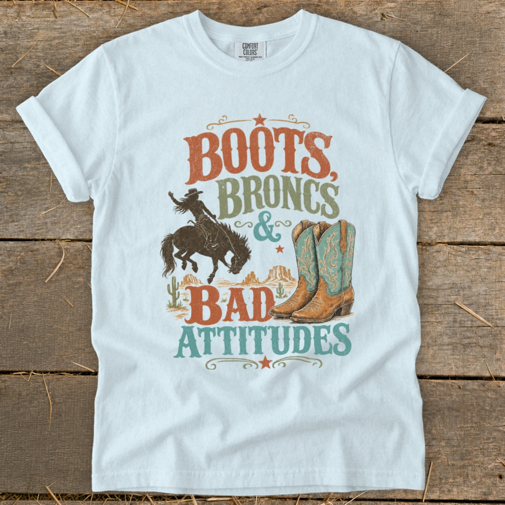 White t-shirt with "Boots, Broncs & Bad Attitudes" graphic featuring a rodeo rider and cowboy boots.