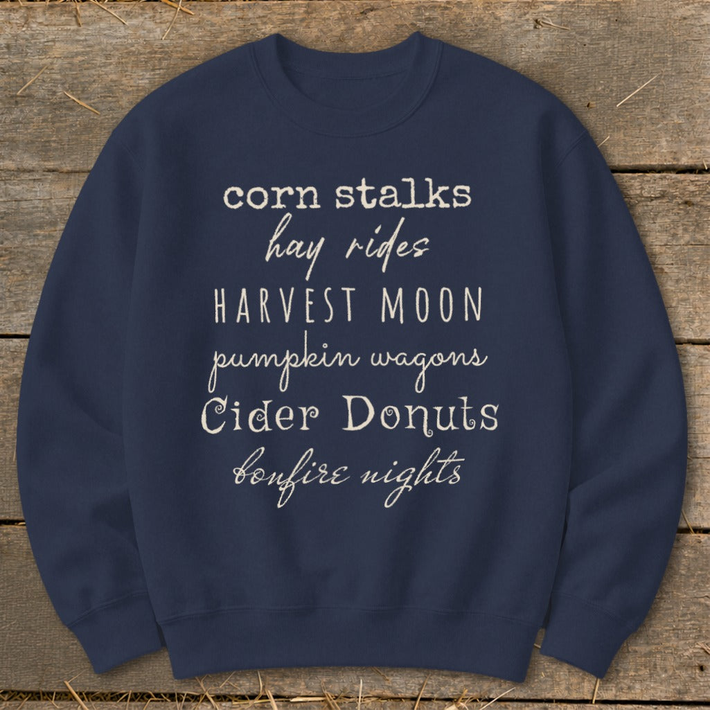 Navy sweatshirt with text listing autumn activities: corn stalks, hay rides, harvest moon, pumpkin wagons, cider donuts, bonfire nights.